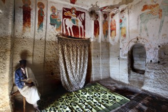 Priest sits in the richly decorated rock church Abba Daniel Krokor, zero