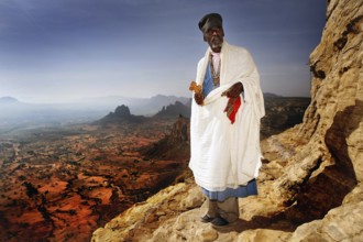 Abba Tesfay in traditional clothing with a view of the expanse of the Gheralta Mountains, Gheralta