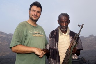 Police officer Muhammed stands next to a man in the volcanic landscape of Erta Ale, Erta Ale, Afar,
