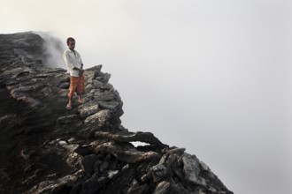 Mountain guide stands at the edge of a smoking crater in a foggy atmosphere, zero