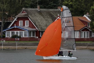 Sailing boat with glowing sail in front of traditional wooden house, Pervalka, Neringa, Lithuania