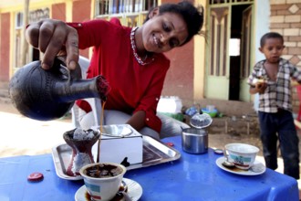 Woman preparing coffee ceremony in Mayzebri, Ethiopia while a child watches, Mayzebri, Ethiopia