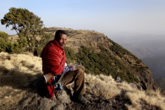 Armed companion sits in the impressive landscape of Semien Mountain National Park, Semien Mountain