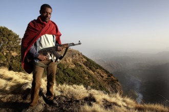 Armed companion stands in front of a vast mountain panorama in Semien Mountain National Park,