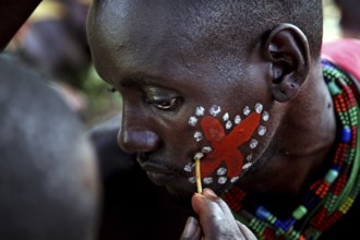 A hamer receives elaborate red and white face painting as part of an initiation ritual, Turmi,