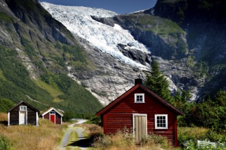 Red and white huts in front of the majestic Bøyabreen Glacier Range, surrounded by green mountains,
