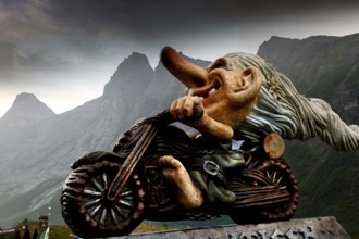 Sculpture of a troll on a motorcycle, against a picturesque mountain backdrop, Trollstigen, Møre og