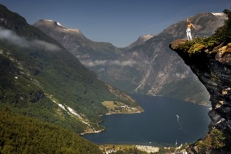 Adventurous tourist stands on cliff and enjoys views of Geirangerfjord, Flydalsjuvet,