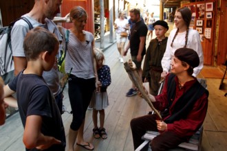 People in historical costumes interact with tourists in a wooden house alley, Bergen, Norway
