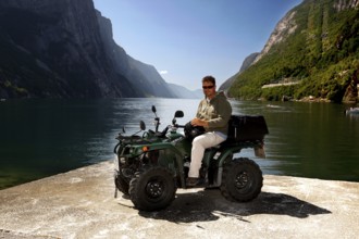 Man on ATV at water with mountains in background in Lysefjord, Lysebotn, Rogaland, Norway