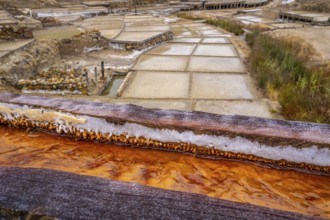 Salt crusts and mineral deposits visible on wooden channels carrying saline water to evaporation