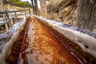 Brine rich in iron and minerals flows through a wooden channel at the ancient salt flats of anana