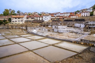 Ancient salt pans and evaporation terraces, with traditional village buildings in the background,