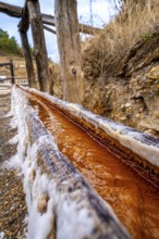 Close up view of the reddish brine flowing along a wooden channel encrusted with salt deposits at