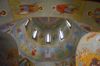 Colourful frescoes in a church dome depicting biblical scenes and angels around windows, domed