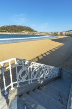 Scenic view looking down ornate white railings and stairs to the wide sandy beach of la concha bay,