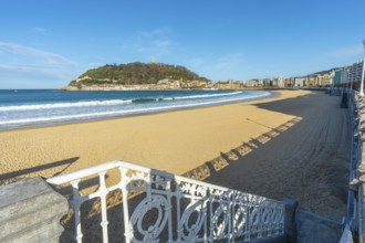 La concha beach view with its iconic promenade railing, golden sand and the city of san sebastian