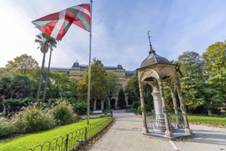 Basque ikurrina flag waving over historic gipuzkoa square in san sebastian, framed by lush gardens,