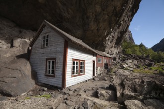 Historical wooden houses sheltered under a massive rock overhang. Summer, Helleren (Helleren),