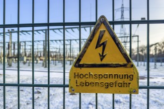 Recording of snow in winter warning sign warning high voltage danger to life on fence from behind