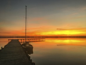 Tranquil Dümmer See with dock and sailboat at sunset, warm colors and calm atmosphere, Lembruch,
