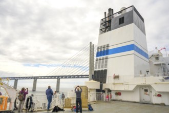 Passengers on a ship with a view of the Øresund Bridge, a ferry under a massive bridge structure of
