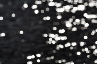 Abstract black background, sparkling white lights, bokeh balls, light reflections on water surface,