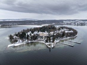 The wintry and snowy Mainau island in Lake Constance with the pier and the baroque Mainau Castle,