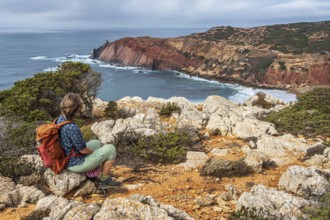 Hiking woman takes a break, view over cliff, Fishermens Trail, Rosa Vicentina, western Algarve just