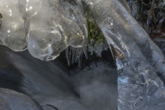 Branches are covered with ice near the river. The water flows gently and forms ice formations on