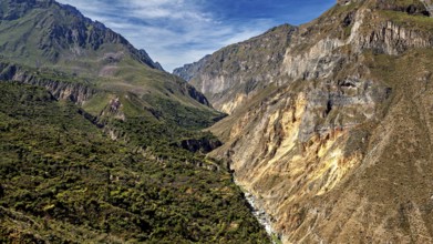 Narrow river snakes through a deep gorge between green mountains, the landscape of Colca Canyon in