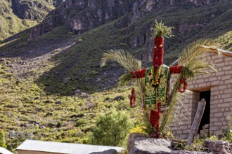A scarecrow decorated with traditional costumes stands in a sunny mountain landscape next to a