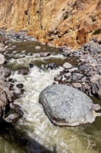 Close-up of a torrential river surrounded by boulders and orange cliffs, The landscape of the Colca