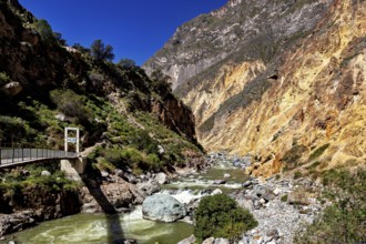 Narrow bridge across river flanked by steep rock walls under deep blue sky, the landscape of Colca