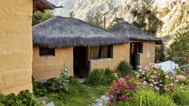 Rustic clay huts with thatched roofs in a blooming, mountainous landscape under bright sunshine,