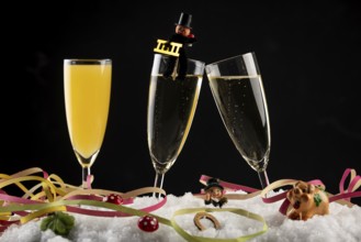 Three champagne glasses with lucky charms for the New Year and streamers in the snow