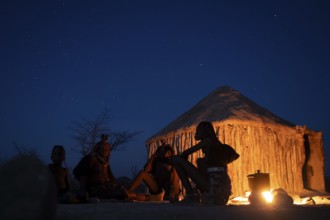 Himba at the campfire in the evening, night view, Himba huts, traditional Himba village in the