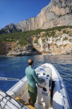 Young man rides a motorboat along the picturesque rocky coast, cliffs and blue sea, Golfo di