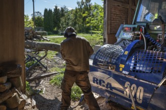 Young man sawing and splitting beech logs with his saw cutting machine, powered by a tractor in a