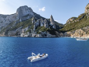 Motor boat off picturesque rocky coast, cliffs with L'Aguglia pinnacle, blue sea and Cala Goloritzé