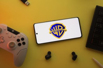 Dhaka, Bangladesh- 22 Mar 2025: Smartphone with Warner Bros. Games, game controller, and earbuds on