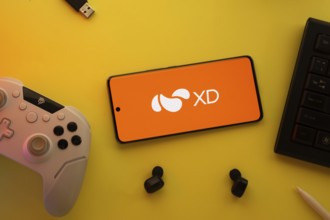 Dhaka, Bangladesh- 22 Mar 2025: Smartphone with XD logo, game controller, and earbuds on a pink