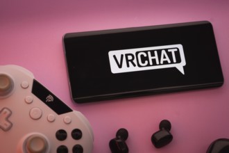 Dhaka, Bangladesh- 22 Mar 2025: Smartphone with VRChat logo, game controller, and earbuds on a pink