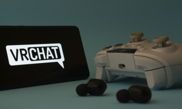 Dhaka, Bangladesh- 23 Mar 2025: A smartphone with a VRChat icon next to a controller and earbuds on