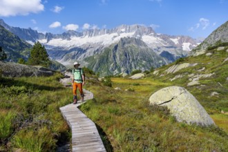 Mountaineers on wooden plank trail through mountain moor, in front of picturesque mountain scenery,