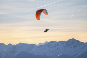 Paragliders flying over snowy mountain peaks in winter in evening light, Kitzbühel Alps, Tyrol,