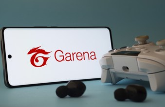 Dhaka, Bangladesh- 23 Mar 2025: A smartphone with a Garena icon next to a controller and earbuds on