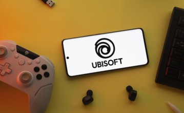 Dhaka, Bangladesh- 23 Mar 2025: Smartphone with Ubisoft logo, game controller, and earbuds on a