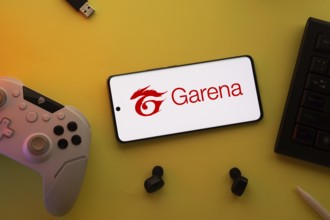 Dhaka, Bangladesh- 23 Mar 2025: Smartphone with Garena logo, game controller, and earbuds on a