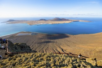 View of La Graciosa island with volcanic craters in the evening light, tourists on an observation